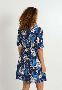 Vestido azul marino con un patrón floral que presenta remolinos en azul, blanco y marrón. Mangas cortas abullonadas y cintura elástica. Textura de tela suave.