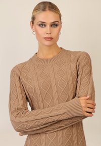 Beige gestrickter Pullover mit einem Kabelmuster, geripptem Ausschnitt und Bündchen sowie einer lockeren Passform. Die strukturierte Oberfläche sorgt für visuellen Reiz.