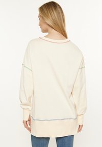 Felpa oversized color crema con maniche lunghe, caratterizzata da cuciture a contrasto in rosso, verde e blu lungo le cuciture e l'orlo.