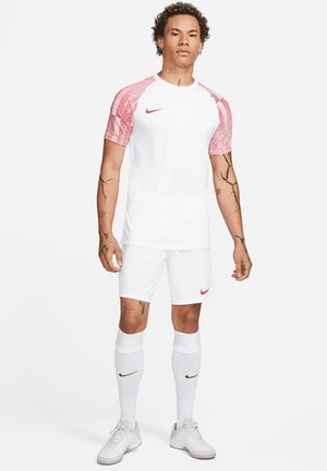 Wit voetbalshirt met korte mouwen en rode gestreepte accenten, gecombineerd met witte shorts en kniekousen. Bevat het Nike-logo in rood en zwart.