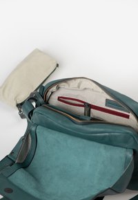 Teal leren tas met een zachte textuur, voorzien van een gestreepte voering, een rode ritszak en een afneembare tas in een contrasterende kleur.