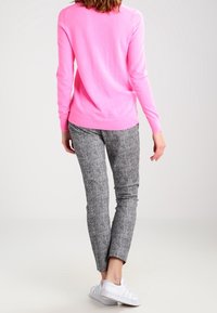Bright pink long-sleeve sweater, lightweight knit; paired with grey textured slim-fit pants and white sneakers. Back view displayed.