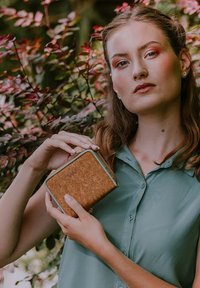 Cork wallet with mint green edging, rectangular shape, zipper closure, held by a person in a light green shirt against foliage background.