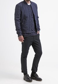 Námořnická prošívaná bomber bunda s žebrovým límcem, vrstvená přes tmavou melírovanou svetr s kulatým výstřihem, doplněná zúženými černými kalhotami a černými botami.