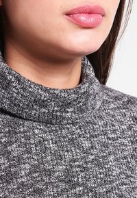Grauer Rollkragenpullover mit strukturiertem Strickmuster, der eine enge Passform und einen umgeschlagenen Kragen aufweist. Glattes Material mit weichem Finish.