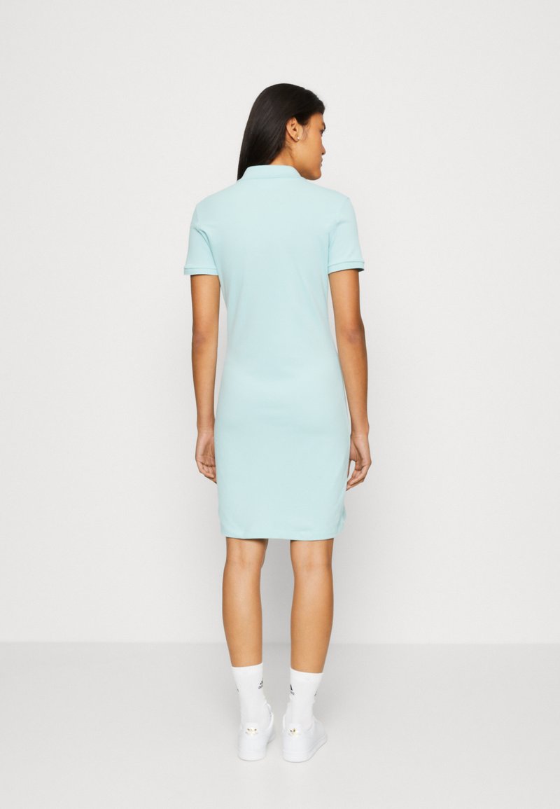 Abito polo azzurro chiaro con maniche corte, taglio al ginocchio e tessuto morbido. Indossato con sneakers bianche e calzini alla caviglia.