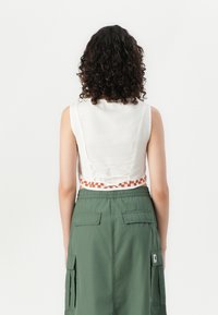 Geknipte witte top met een geweven oranje accent bij de taille, gecombineerd met een lange groene cargorok met zijzakken en een elastische tailleband.
