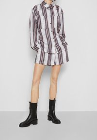 Chemise à rayures en tissu léger avec deux poches poitrine, associée à un short assorti. Bottines noires à talons épais.