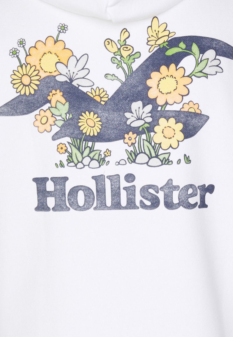 Weißer Hoodie mit floralem Design in Gelb, Grün und Blau sowie einem dunkelblauen Logo "Hollister" am unteren Rand. Weicher Stoff, lässiger Stil.