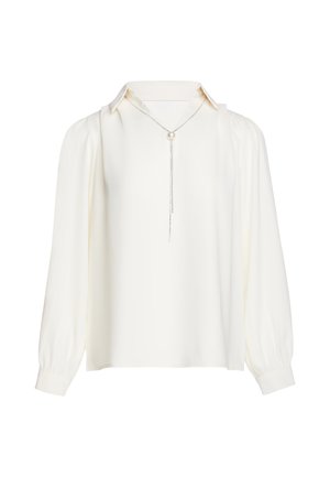 Blouse blanche à manches longues avec un col pointu et un collier en argent avec une perle centrale et des chaînes pendantes.
