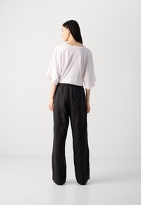Witte, kortgemouwen top met een ronde hals, gecombineerd met losse, zwarte linnen broek met een achterzak.