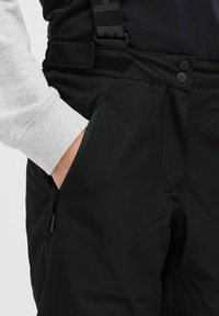 Black ski pants with a smooth texture, adjustable straps, two button closures, and a zipper pocket on the side.