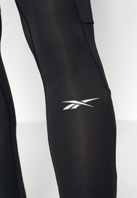 Svarta leggings i stretchmaterial. Utrustade med en vit logotyp p å underbenet och kontrasterande sömdetaljer längs sidorna.