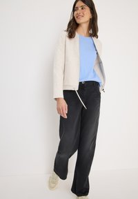 Lichtbeige ritsjack, blauwe t-shirt, zwarte wijde broek en beige sneakers, met een soepele stoftextuur en een minimalistisch ontwerp.
