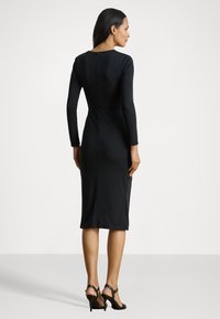 Černé dlouhé šaty s upnutou siluetou, délka ke kolenům a zapínání na skrytý zip vzadu. Hladká textura a elegantní designové detaily.