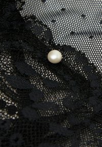 Zwarte kant stof met bloemmotieven, met een opvallende witte parel als accent. Gelaagd en delicaat, met een fijne gaasuitstraling.
