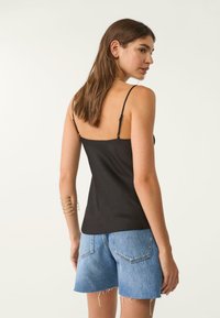 Schwarzes Camisole-Top mit dünnen verstellbaren Trägern, kombiniert mit hellblauen, ausgewaschenen Denim-Shorts mit fransigen Säumen und Gesäßtaschen.