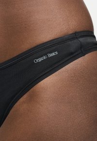 Gros plan d'une peau foncée portant des sous-vêtements noirs avec le logo « Organic Basics » sur la ceinture.