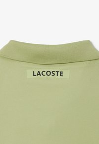 Polo de color verde claro con cuello acanalado y etiqueta con el logo de Lacoste en negro. Tejido texturizado con un acabado suave.