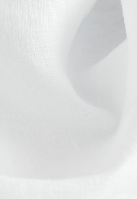 Gros plan d’un tissu en lin blanc montrant sa fine texture tissée et ses plis doux.