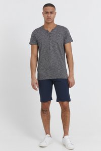 Grå melange kortærmet henley-shirt med knaplukning i halsen, parret med navy shorts. Båret med hvide sneakers. Synlig tatovering på benet.
