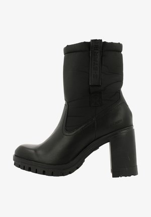 Zwarte enkelboot met hak, voorzien van een gevoerde textielen bovenkant, een ronde neus en een rubberen loopzool. Voorzien van een logo-accent en een trekhaak voor eenvoudig aan- en uittrekken.