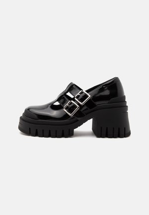 Chaussure noire en cuir verni à talon épais, double boucle argentée et semelle épaisse rainurée, vue latérale sur fond uni.