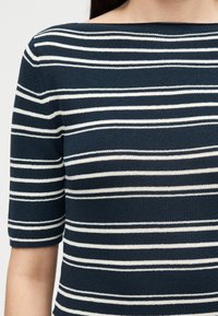 Πλεκτό μπλε ναυτικού χρώματος τοπ με ομοιόμορφα κατανεμημένες λεπτές λευκές οριζόντιες ρίγες και κοντά μανίκια, εμφανιζόμενο στο πάνω μέρος του κορμού και την περιοχή των ώμων.