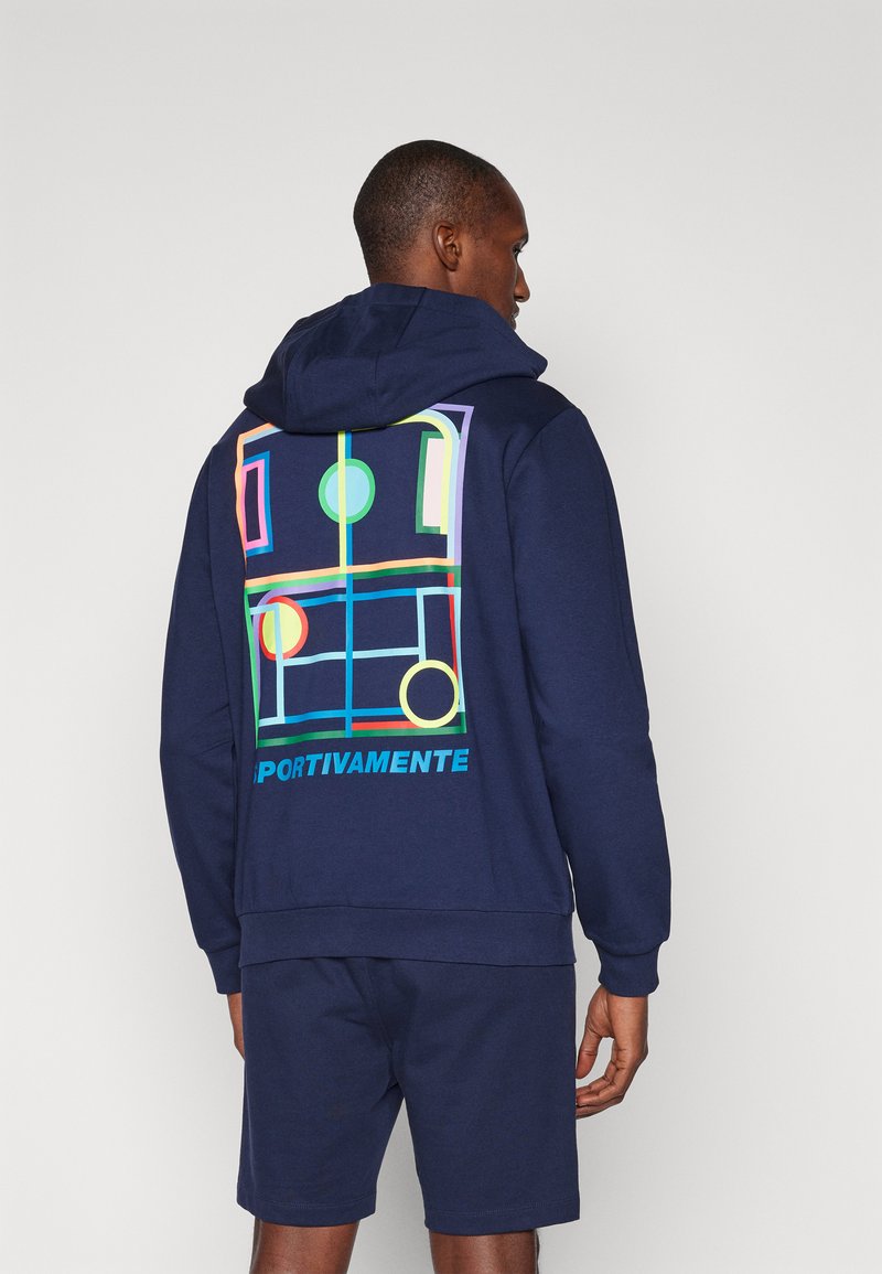 Mørkeblå hoodie i blødt materiale har et grafisk design med farverige former på ryggen, herunder cirkler og rektangler, samt tekst.