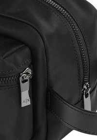 Borsa nera in nylon con una superficie liscia, dotata di chiusura con zip e accessori in argento lucido con logo inciso. Design compatto con tasca laterale.