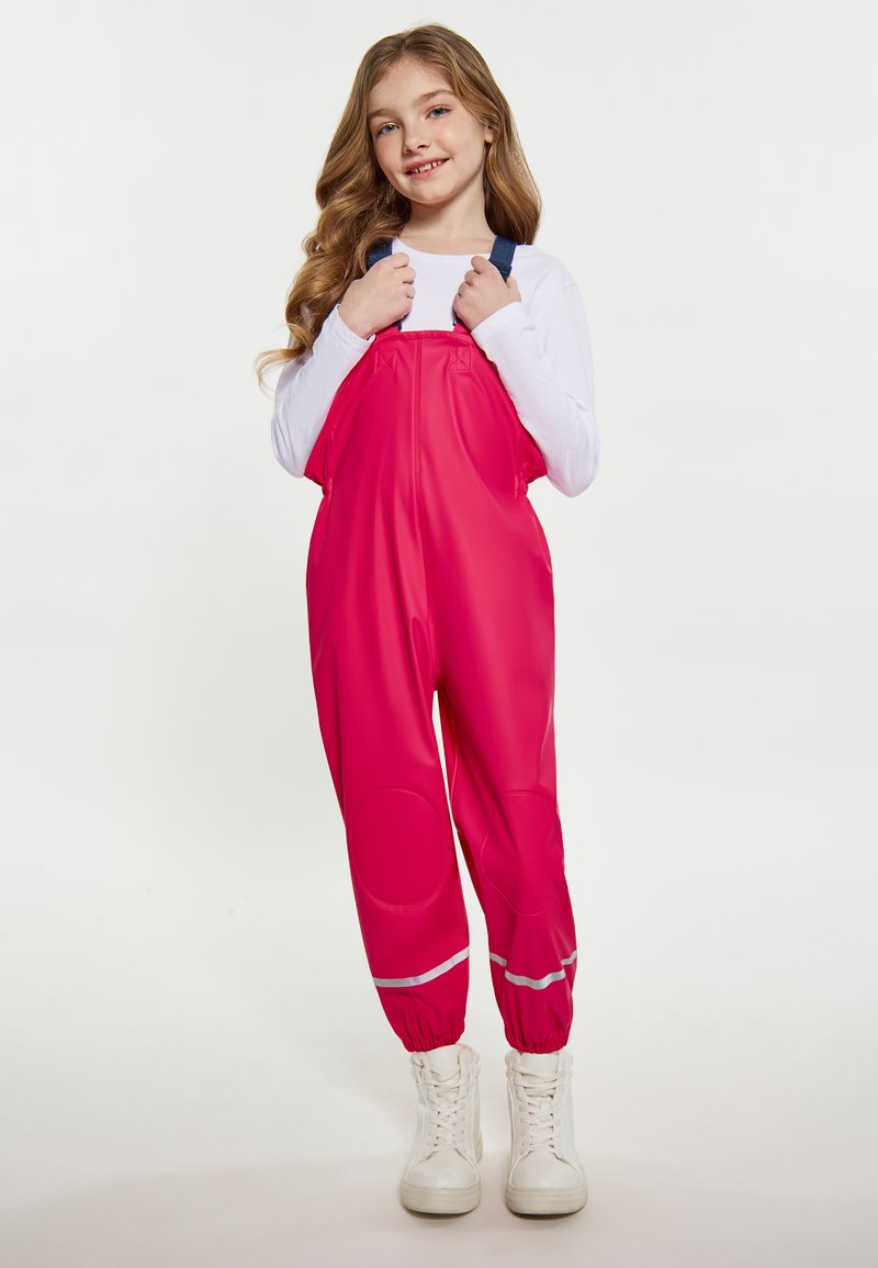 Jasne ružové nepremokavé nohavice s nastaviteľnými modrými popruhmi, elastickými manžetami a reflexným pruhovaním. Nosia sa cez biele tričko s dlhým rukávom.