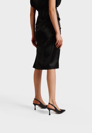 Décolleté slingback nere con punta a punta con finitura lucida, tacchi sottili, cinturino alla caviglia e design con taglio aperto che mette in mostra una silhouette elegante.