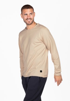 Beige Langarmshirt mit Rundhalsausschnitt und lockerer Passform. Mit einem kleinen schwarzen Logopatch am Saum und einem glatten, leichten Stoff.