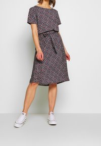 Robe florale noire avec des manches courtes, une taille à nouer et une longueur jusqu'aux genoux. Le matériau présente une texture douce avec de petites fleurs multicolores.