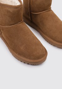 Les bottes chelsea en daim marron présentent une doublure intérieure douce, un bout arrondi et une semelle en caoutchouc texturée, avec des détails de couture autour du tige.