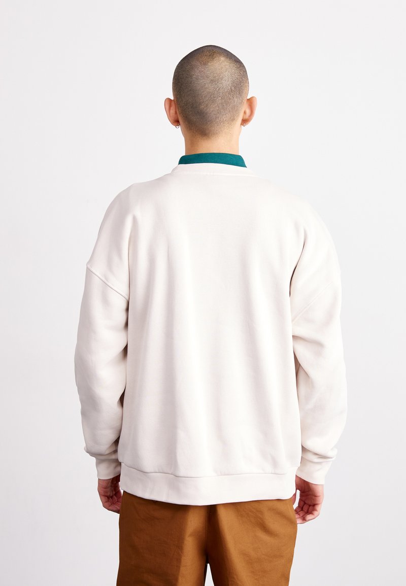 Sweatshirt crème avec une coupe décontractée, col côtelé vert et poignets élastiques. Fabriqué en tissu doux, il présente un design épuré et minimal.