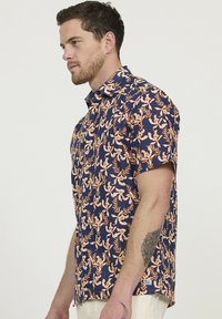 Kortebloemig overhemd in marineblauw met oranje bloemenpatroon, voorzien van een button-down kraag en een relaxte pasvorm, gemaakt van lichte stof.