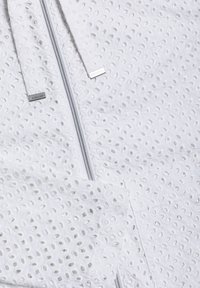 Hvidt stof med et ålægs mønster har en sølvlynlås og to snore, hver med små metalender med mærke.