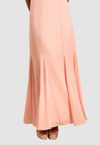 Maxikleid aus weichem Pfirsichstoff mit ausgestelltem Saum und gefalteten Details, kombiniert mit tanfarbigen Plateausandalen mit einem Krebsgangriemen-Design.