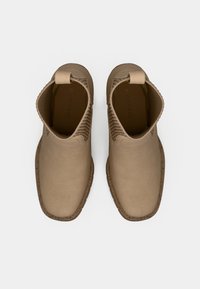 Cizme bej până la gleznă cu un finisaj neted, detalii texturate din elastic cu nervuri în jurul gulerului și o talpă durabilă de tip plută.