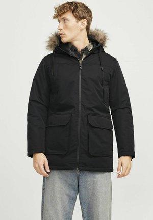 Sort parka med pelsforet hætte, lynlås foran, to store frontlommer og justerbare snore. Blødt, polstret stof med en mat finish.