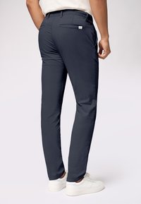 Granatowe slim-fit spodnie z kieszenią z tyłu, wykonane z lekkiej tkaniny, stylizowane z czystym szwem i zwężającą się nogawką, zestawione z białymi sneakersami.