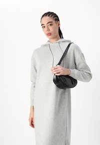 Svijetlosivi dukserica haljina s dugim rukavima i kengur džepom. Crna kožna torba preko tijela zaobljenog oblika s dekorativnim zakovicama.