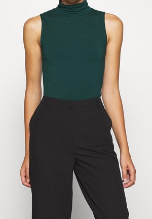 Haut vert sans manches à col roulé, fabriqué en matériau doux, associé à un pantalon noir taille haute. Design simple sans motifs visibles.