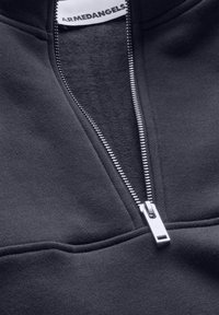 Sudadera con cremallera negra de textura suave, con una cremallera de metal plateado. El interior es suave y está forrado con felpa. Logo visible en la etiqueta.