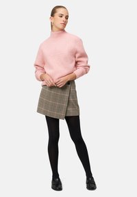 Jasnoróżowy sweter z dzianiny z wysokim kołnierzem, w zestawieniu z brązową spódnicą w kratę, czarnymi rajstopami i czarnymi mokasynami.