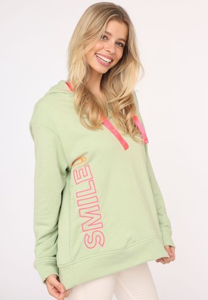 Hellgrüner Hoodie mit pinken Kordelzügen und dem Aufdruck "SMILE!" in kräftigen pinken Buchstaben auf der Vorderseite. Weicher Stoff und lockere Passform.