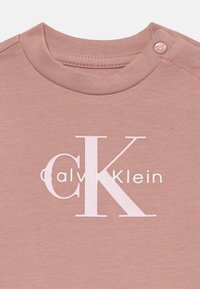 Rozā Calvin Klein bērnu bodijs ar spiedpogu plecā un CK logotipu baltā krāsā uz krūšu daļas.