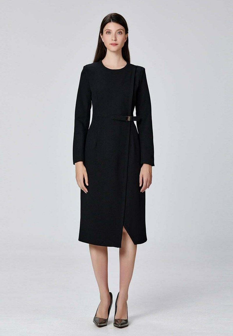 Robe noire à manches longues avec un design habillé, taille ceinturée, silhouette mi-genou et une subtile fente à l'avant. Texture de tissu lisse.