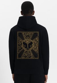Zwarte hoodie met een grote gouden graphic op de rug, featuring abstracte vormen, golven en een centraal embleem. Zacht katoen materiaal, relaxed fit.